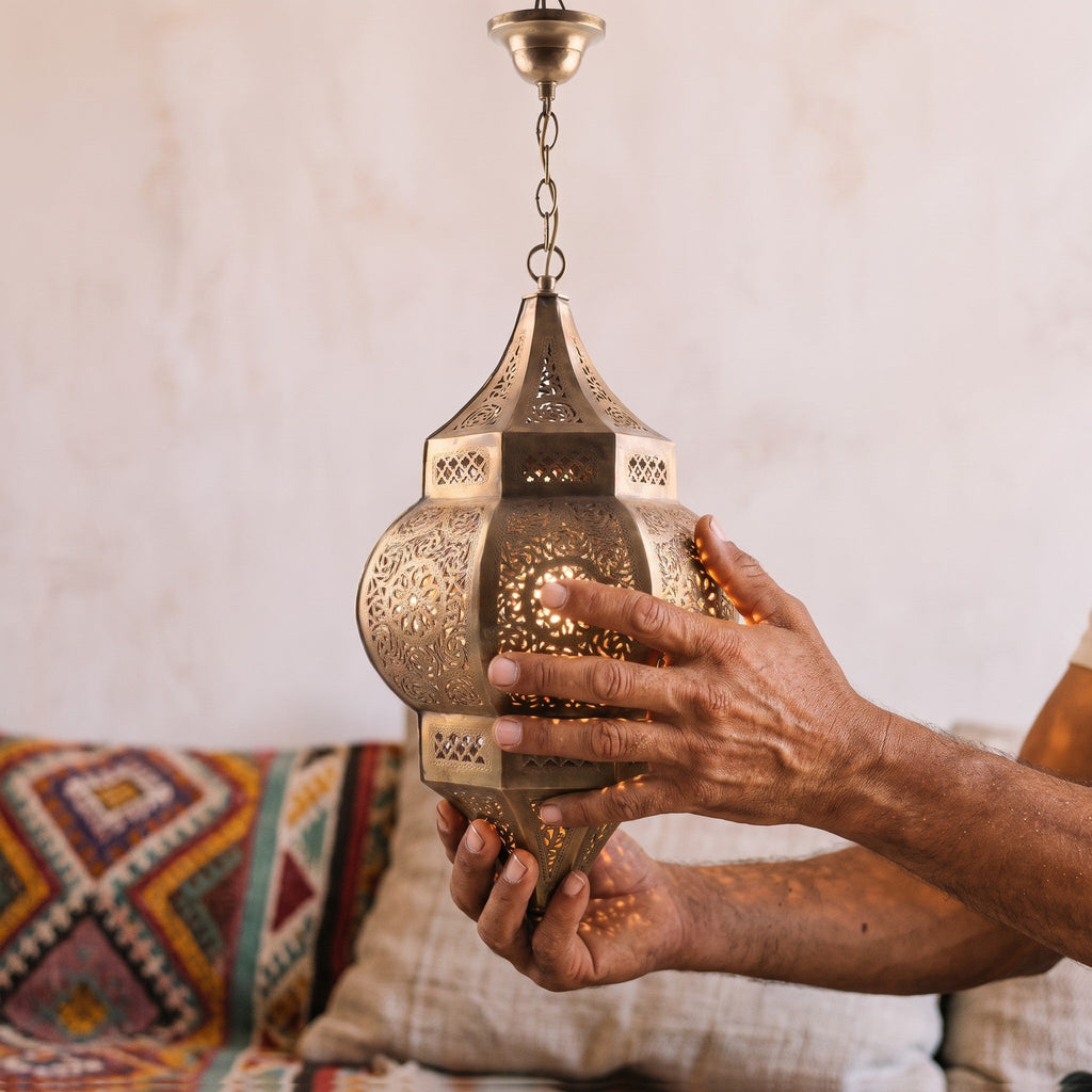 Artisan's hands holding the pierced brass shade of the Amalu sconce