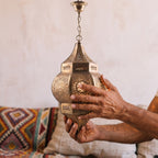 Artisan's hands holding the pierced brass shade of the Amalu sconce