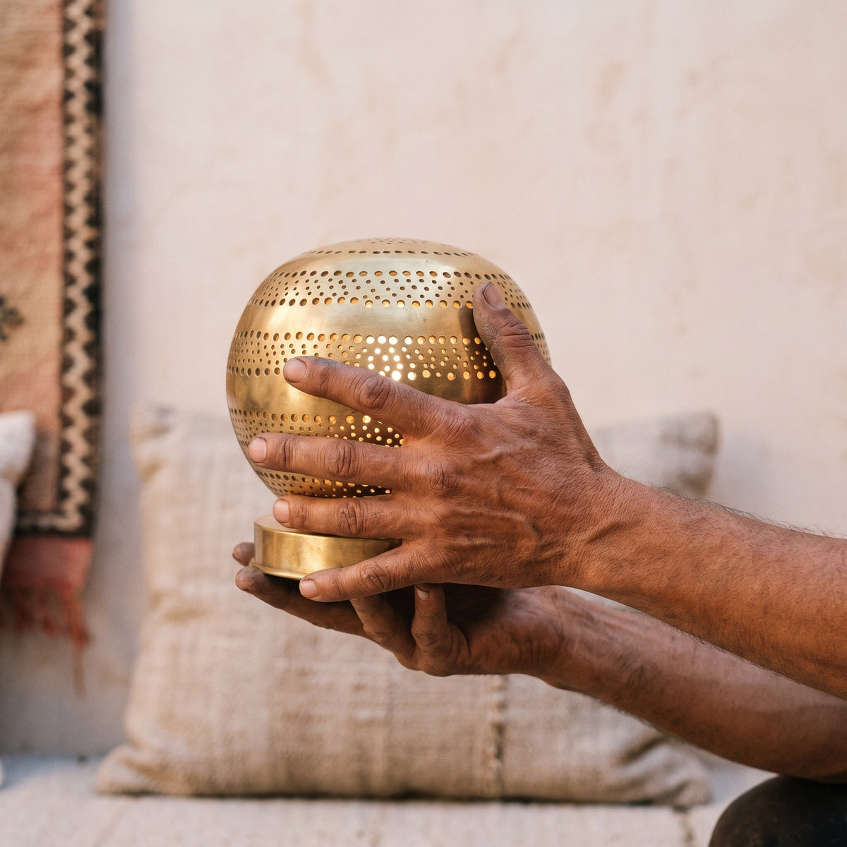 The maker's hands holding the perforated brass sphere of the Aman lamp