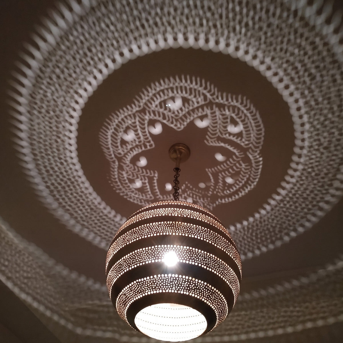 Detail of the lit Amanar pendant, leaf piercings glowing in the brass