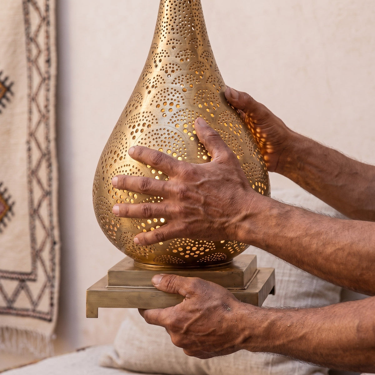 A maalem's hands holding the Anbar brass shade in the Marrakech workshop