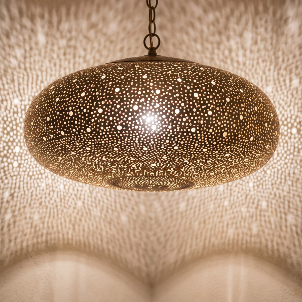 Close view of the lit Anfa pendant, light through the pierced brass