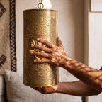 A maalem's hands holding the Aya sconce, pierced Arabic script visible in the brass