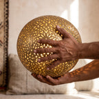The maker's hands holding the engraved brass sphere of the Ayyur lamp