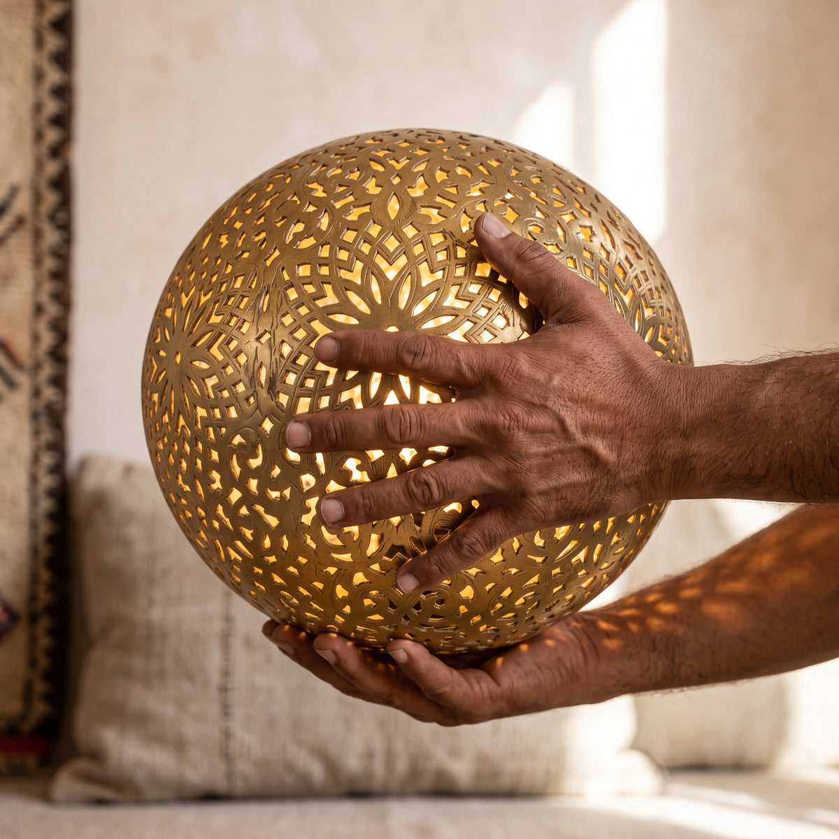 The maker's hands holding the engraved brass sphere of the Ayyur lamp