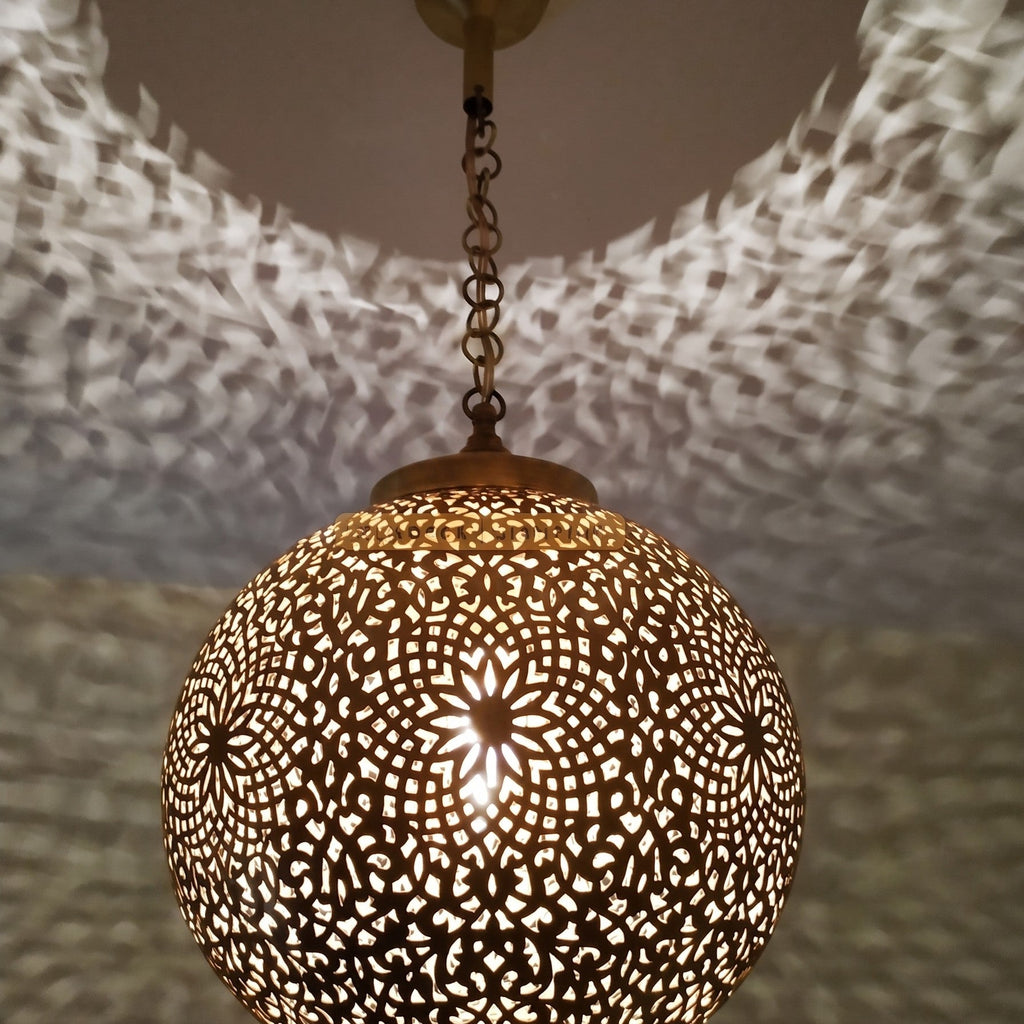 Lit Bahia pendant up close, light passing through the hand-pierced brass motifs