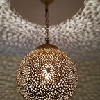 Lit Bahia pendant up close, light passing through the hand-pierced brass motifs