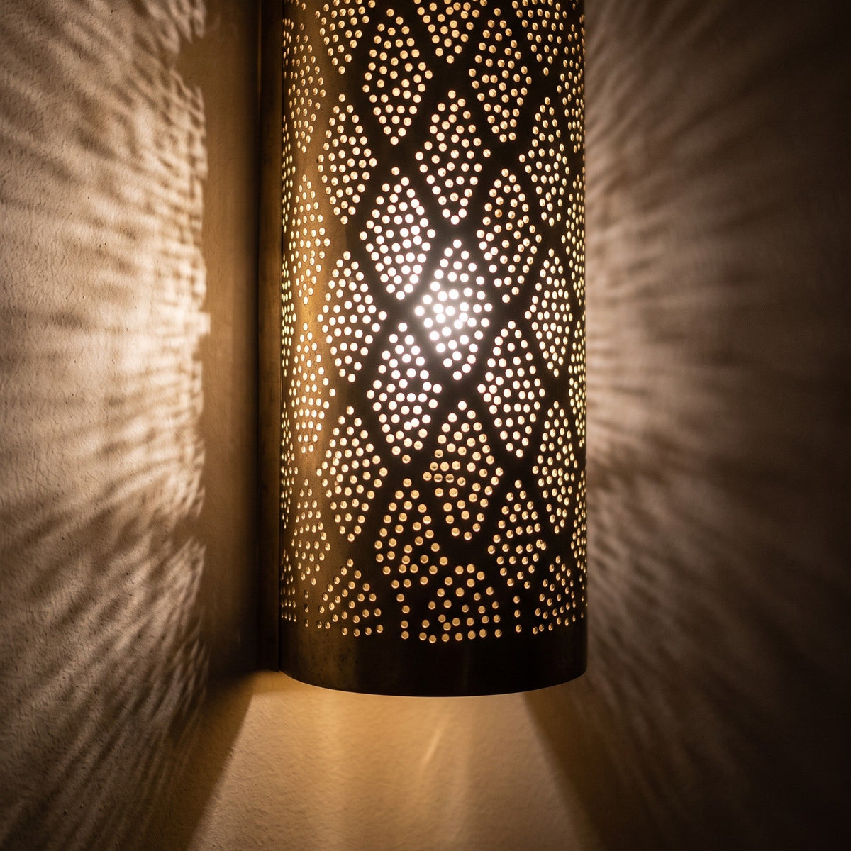 Lit Bahja sconce in close-up, points of light through the pierced brass