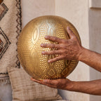 Maker's hands holding the punched brass dome of the Baraka pendant