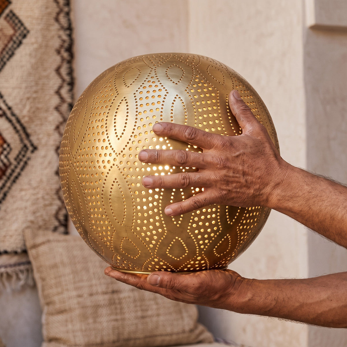 Maker's hands holding the punched brass dome of the Baraka pendant