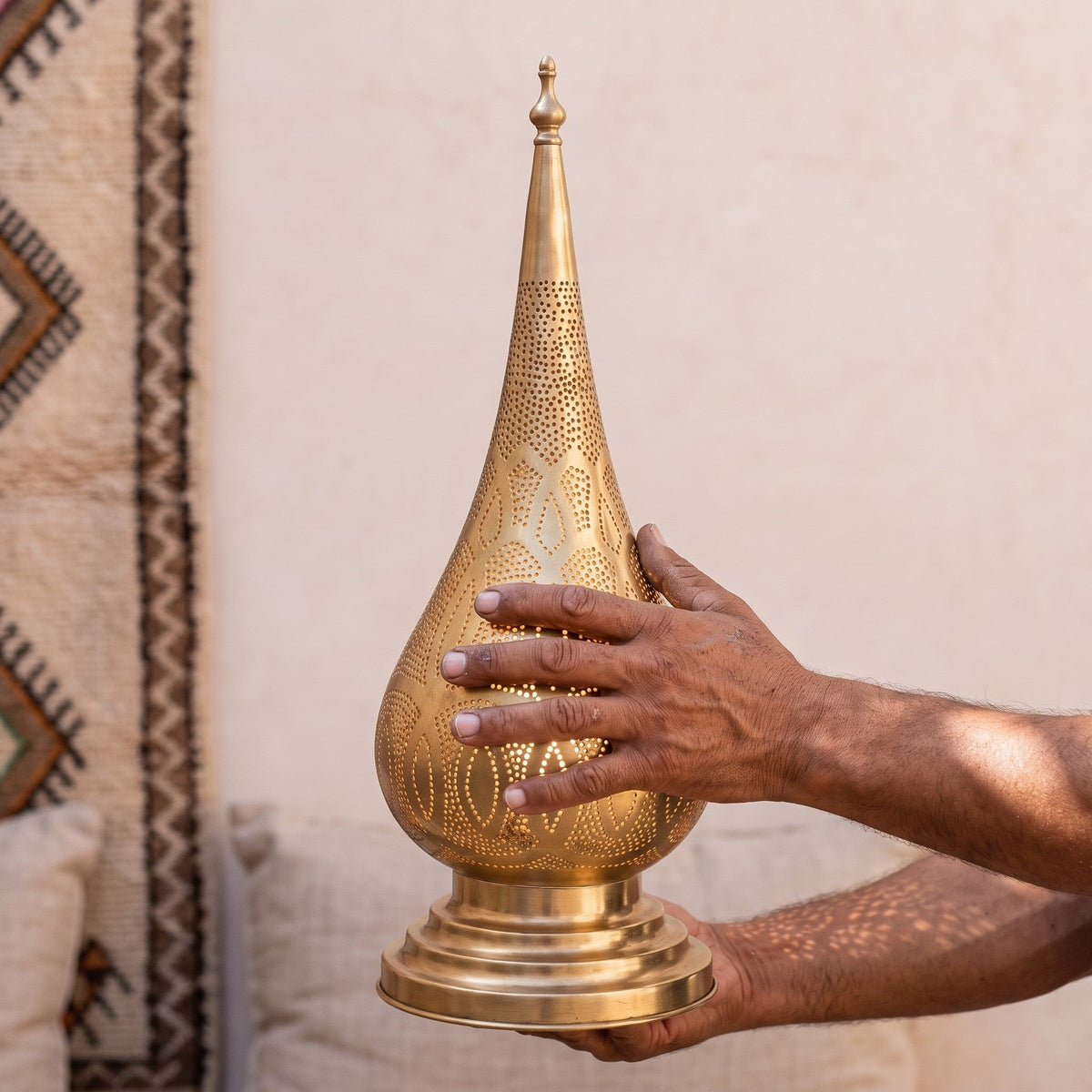 Artisan's hands presenting the pierced brass body of the Dahab lamp