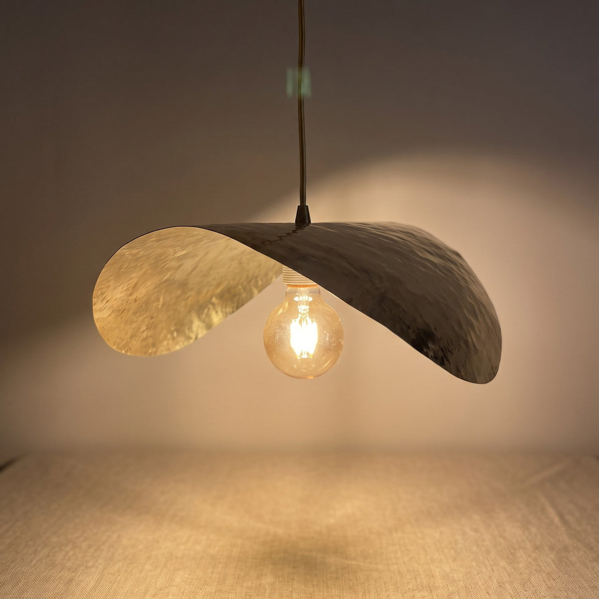 Close detail of the lit Dahbia pendant, warm light on hammered brass