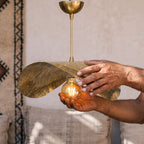 Artisan's hands holding the hammered brass shade of the Dahbia pendant