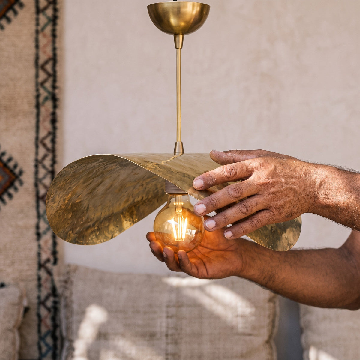 Artisan's hands holding the hammered brass shade of the Dahbia pendant