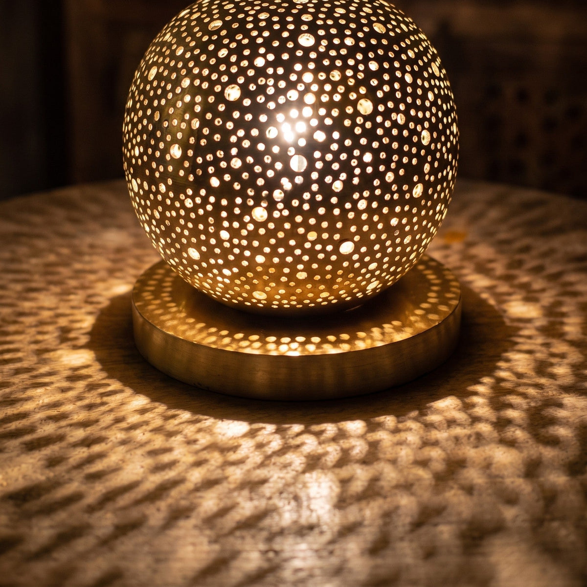 Close view of the lit Daya lamp, small openings glowing across the brass sphere