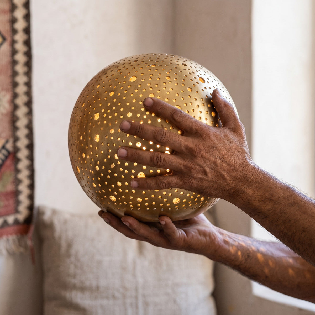 The maker's hands cradling the pierced brass sphere of the Daya lamp