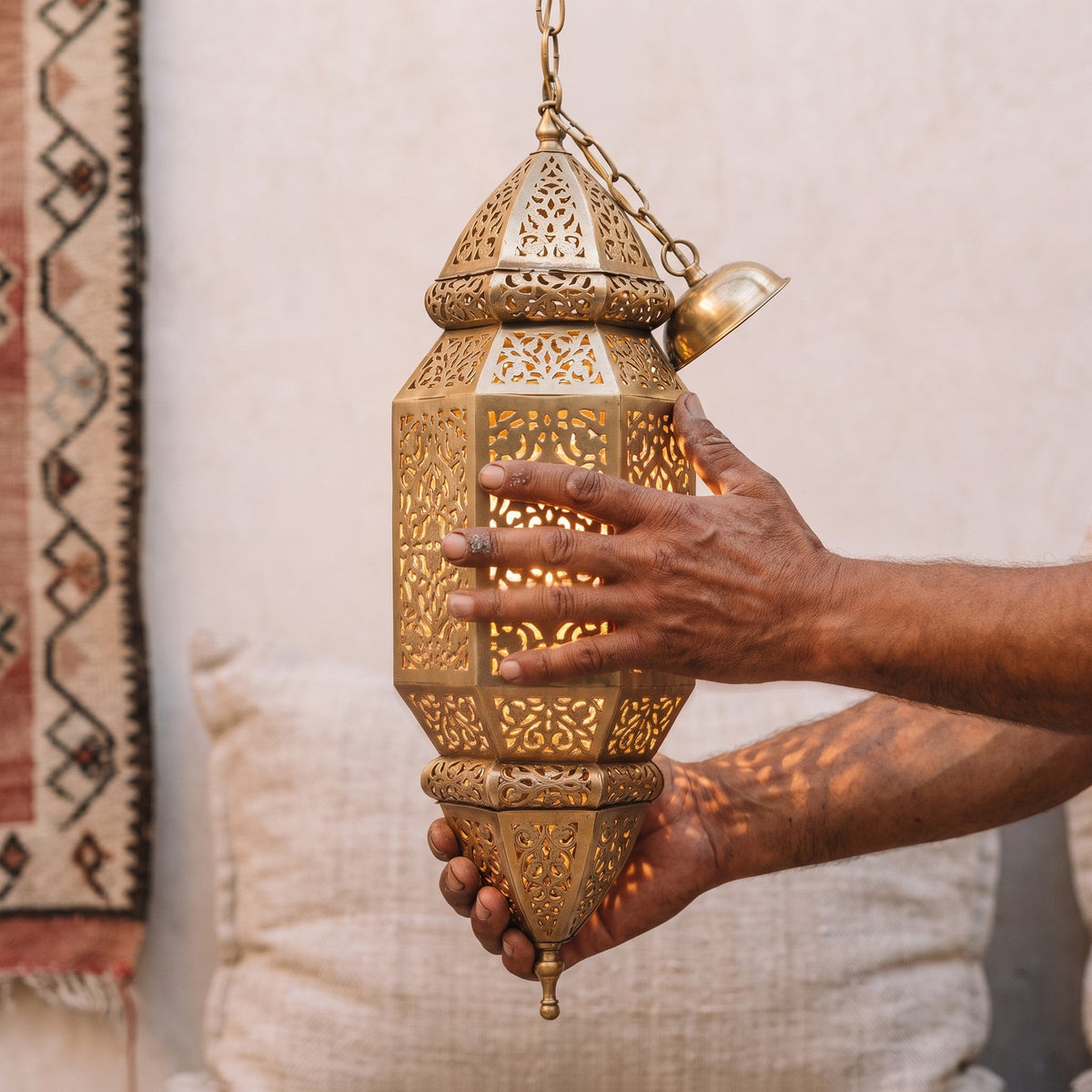 Artisan's hands holding the tall engraved brass body of the Fajr sconce