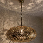 Close view of the lit Gnawa pendant, note-shaped light escaping the pierced brass