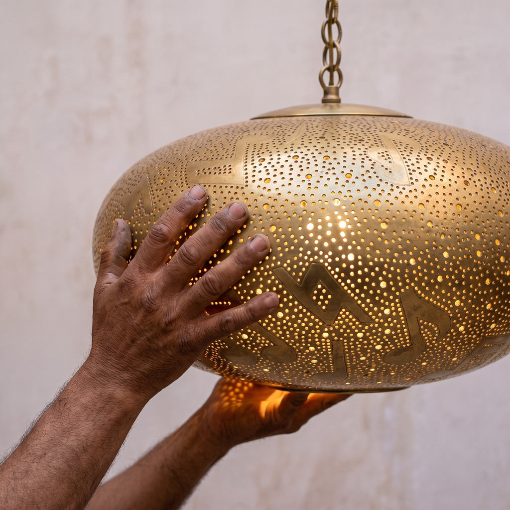 Artisan's hands holding the pierced brass shade of the Gnawa pendant