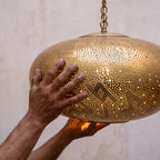 Artisan's hands holding the pierced brass shade of the Gnawa pendant