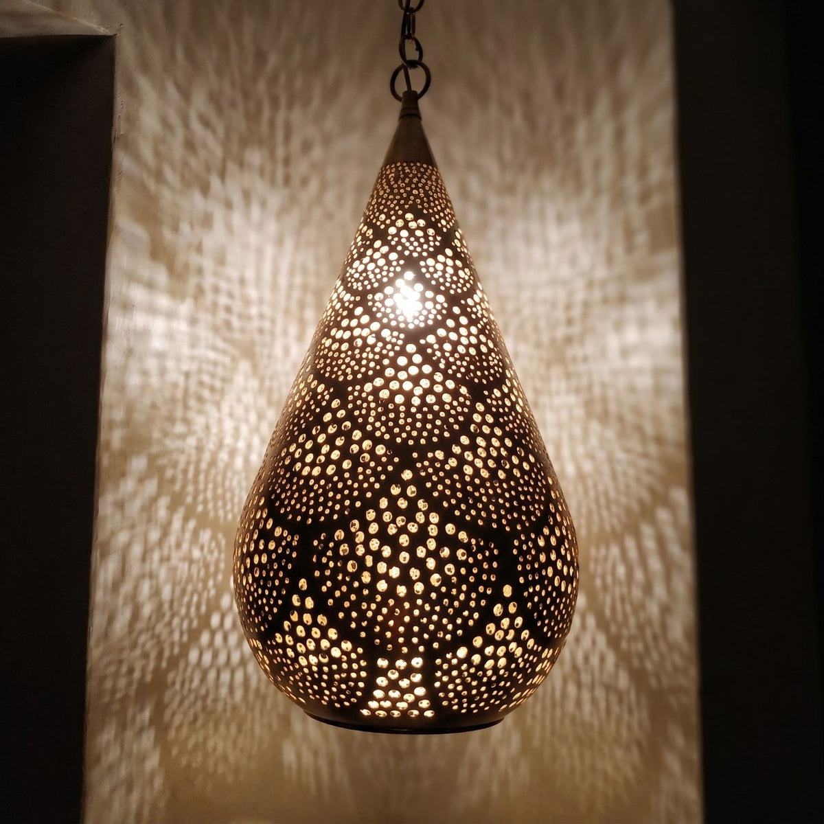 Close view of the lit Itri pendant, light passing through hand-punched circles