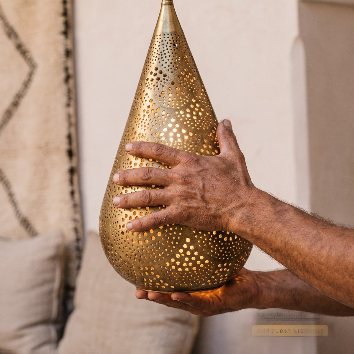 Artisan's hands holding the pierced brass body of the Itri pendant