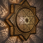 Lit Khamsa sconce up close, small stars of light through the pierced brass