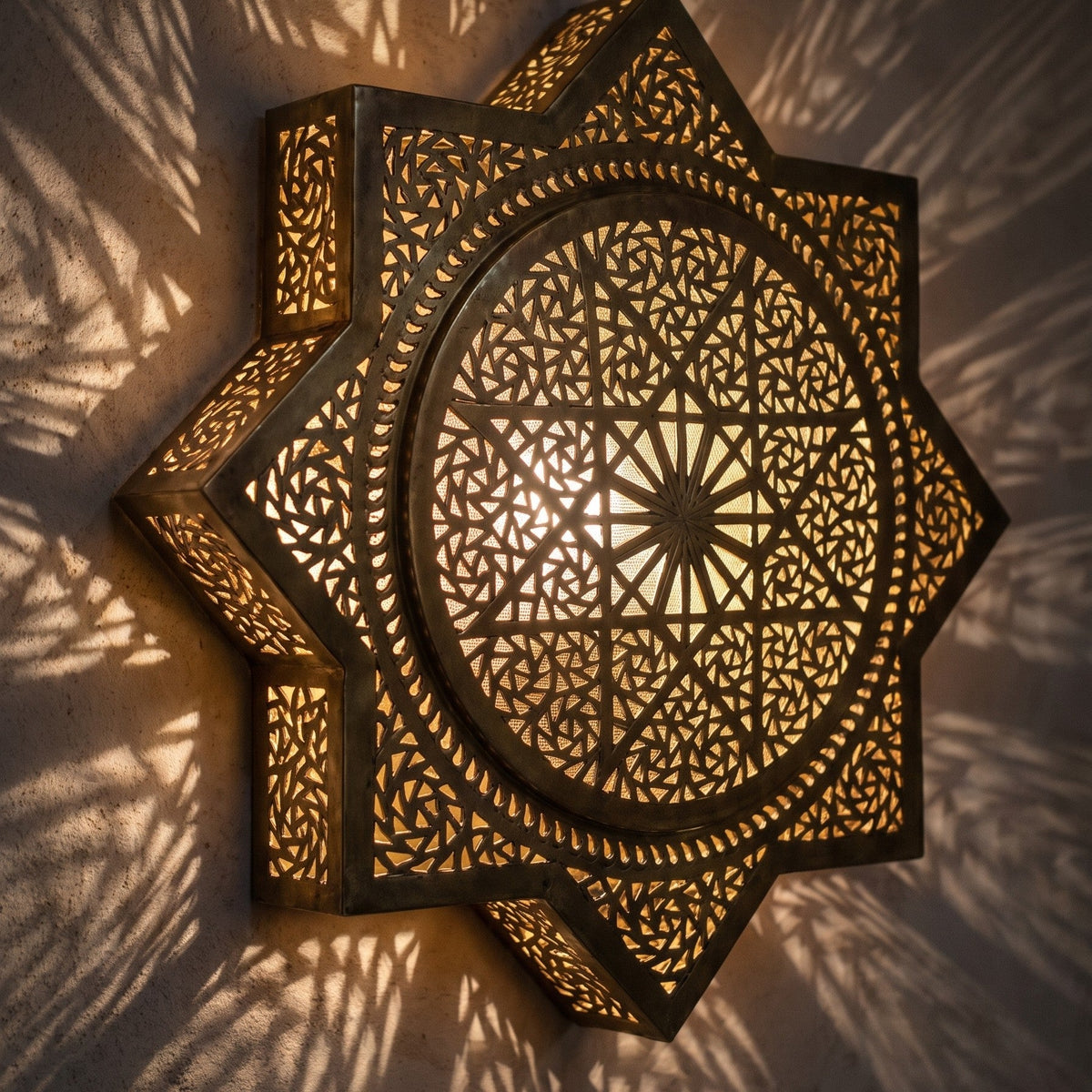 Lit Khamsa sconce up close, small stars of light through the pierced brass