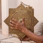 Maker's hands holding the eight-pointed brass body of the Khamsa sconce