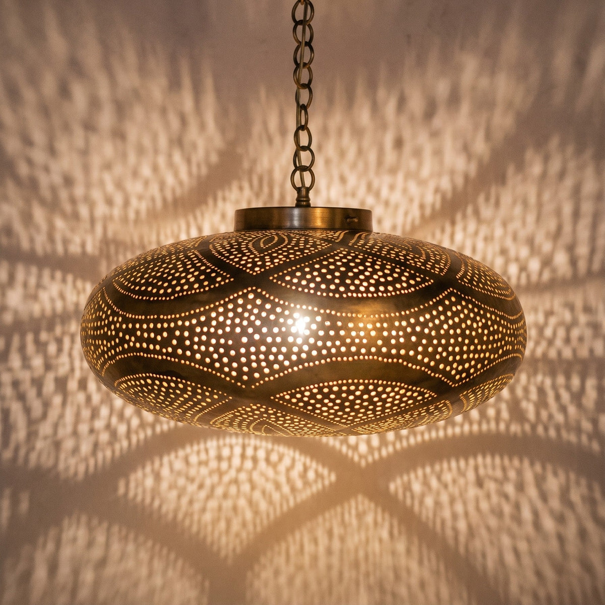 Close view of the lit Layla pendant, leaf pattern glowing through the brass