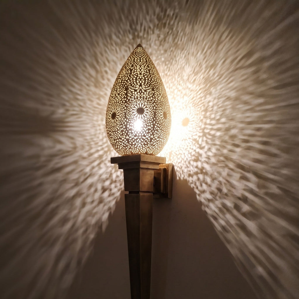Close view of the lit Menara sconce, warm light through hand-pierced openings in the brass