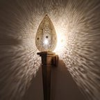 Close view of the lit Menara sconce, warm light through hand-pierced openings in the brass