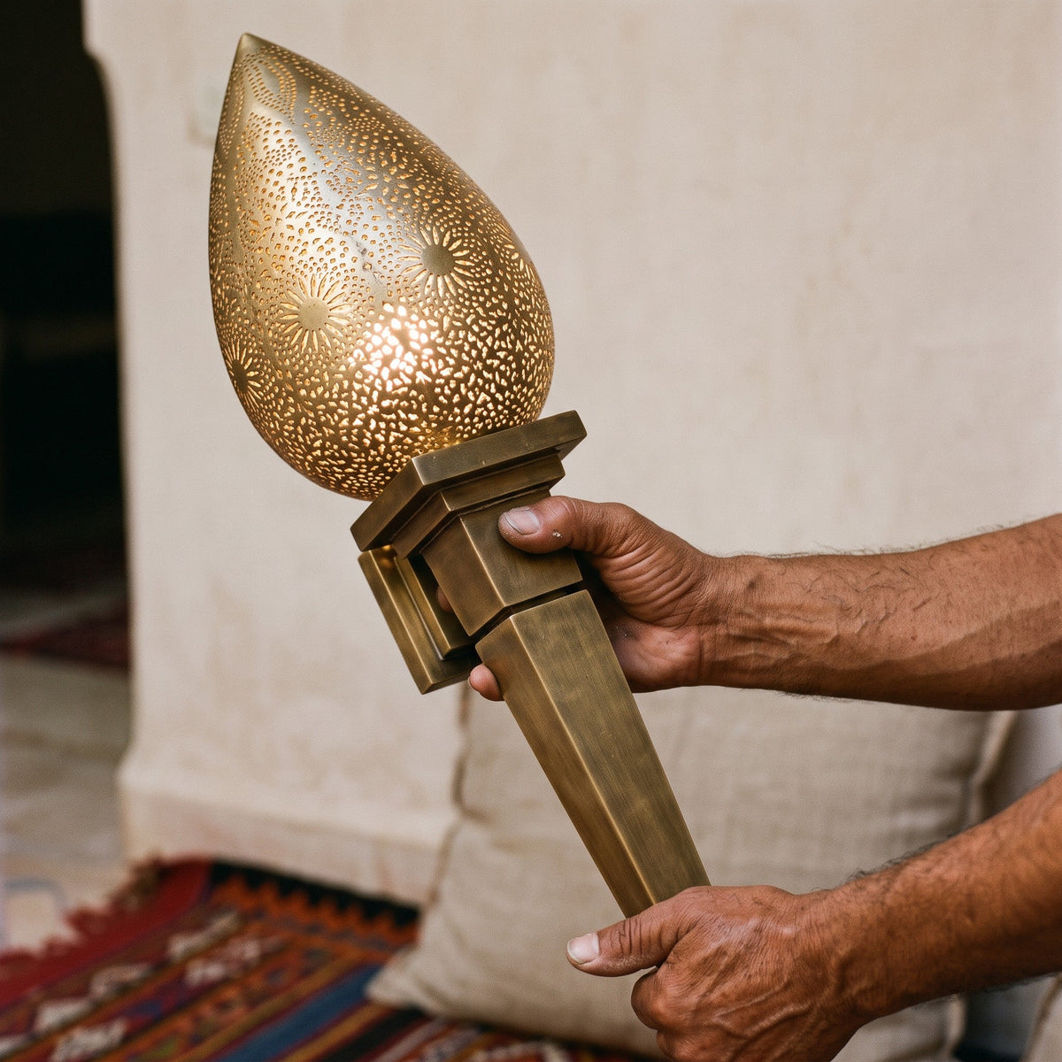 A maalem's hands holding the pierced brass body of the Menara sconce in the workshop