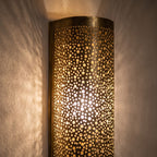 Close detail of a lit Mouassine sconce, warm light through the pierced brass