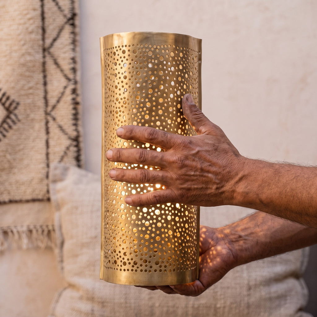 Artisan's hands holding a Mouassine sconce shade, pierced brass catching the light