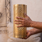 Artisan's hands holding a Mouassine sconce shade, pierced brass catching the light