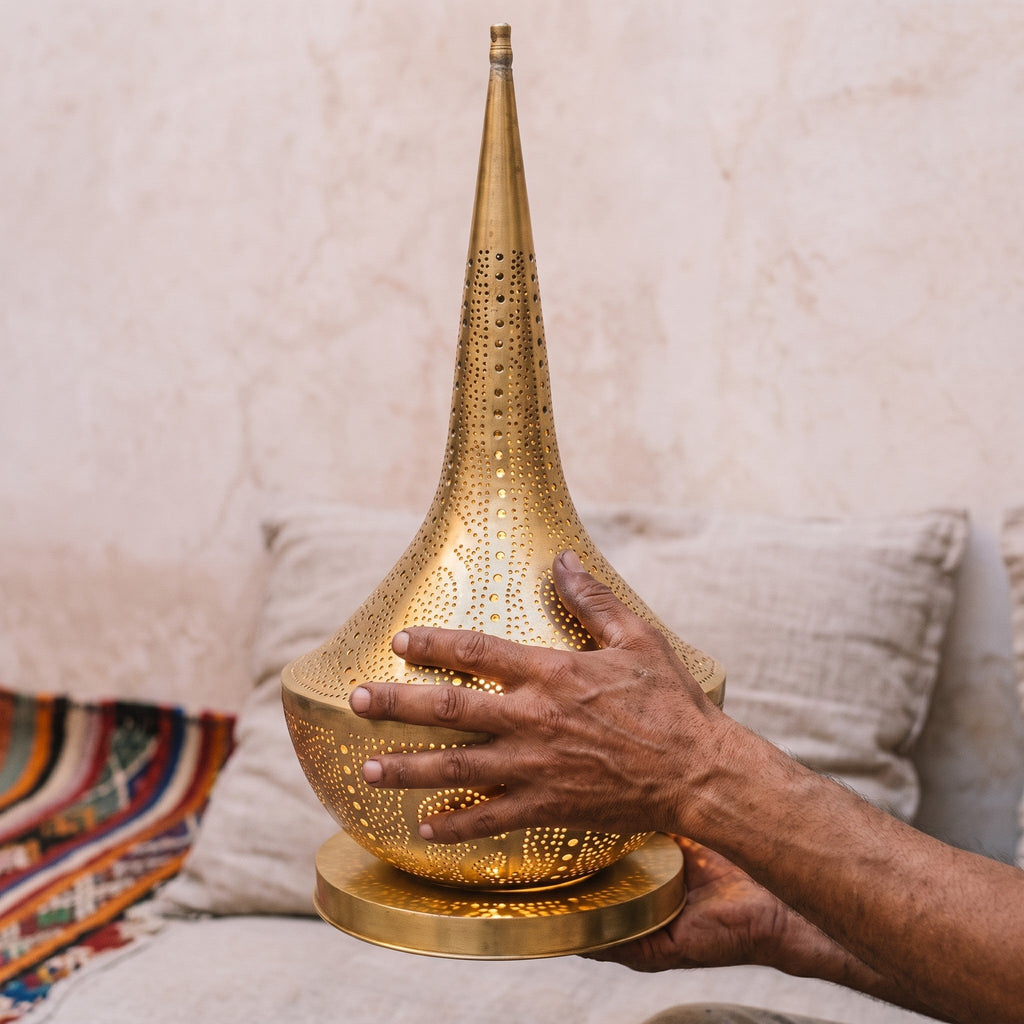 The maker's hands holding the unlit Nassim brass shade, workshop bench behind