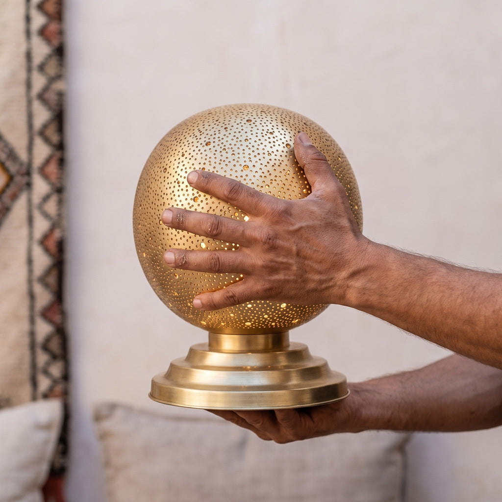A maalem's hands holding the perforated brass globe of the Ourika lamp