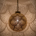 Close detail of the lit Qamar pendant, leaf piercings bright in the brass