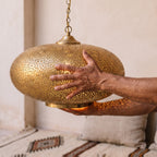 Maker's hands holding the Qandil dome, showing the patina and leaf cuts