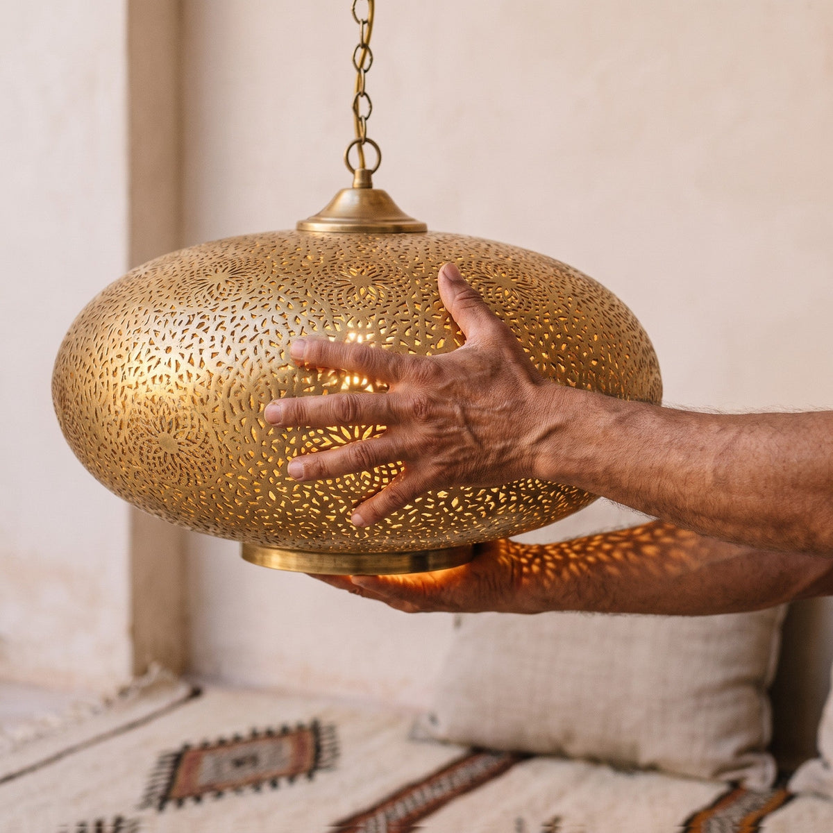 Maker's hands holding the Qandil dome, showing the patina and leaf cuts