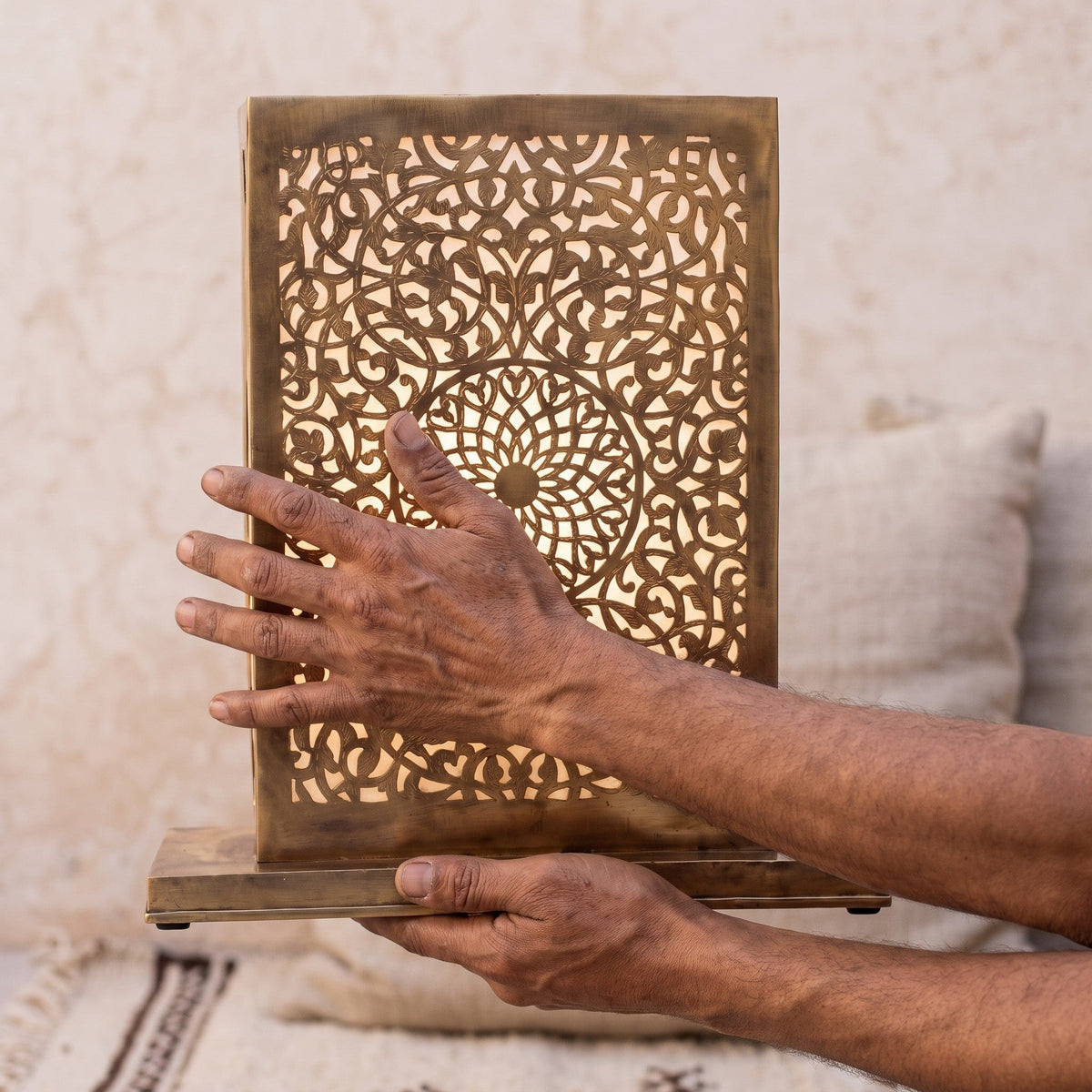 The maker's hands holding the engraved brass disc of the Sabah lamp