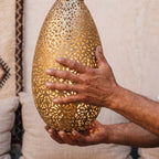 Maker's hands holding the corset-shaped brass body of the Sana sconce
