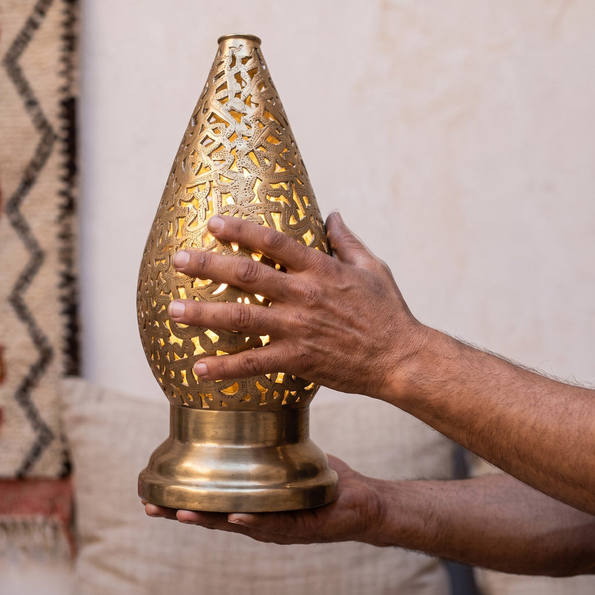 Maker's hands holding one Shama lantern, showing the pierced brass work