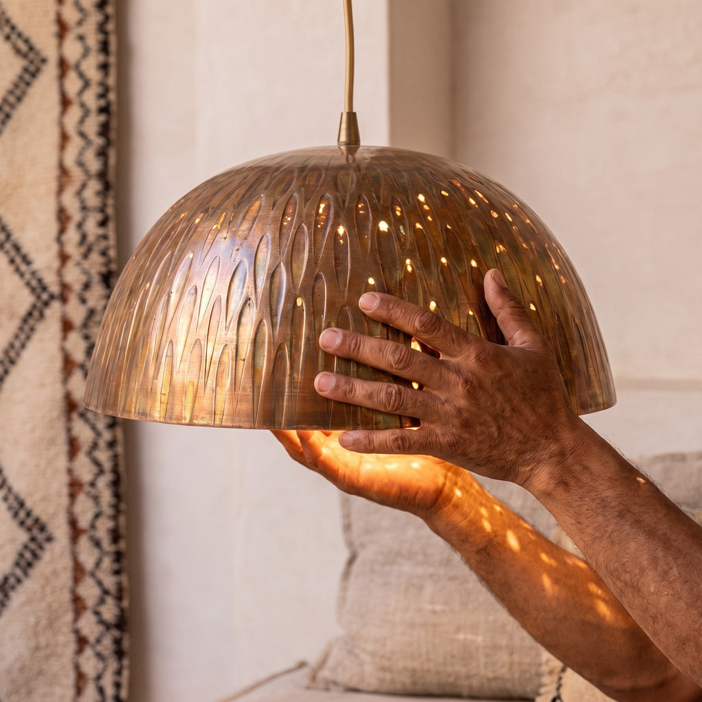 Artisan's hands holding the engraved copper dome of the Siniya pendant