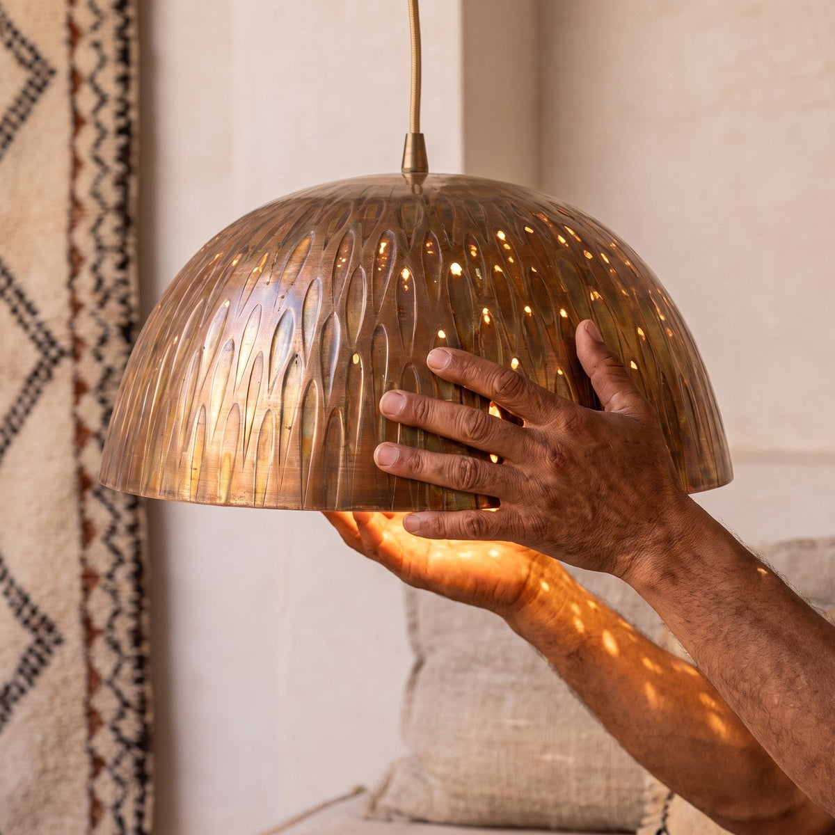 Artisan's hands holding the engraved copper dome of the Siniya pendant