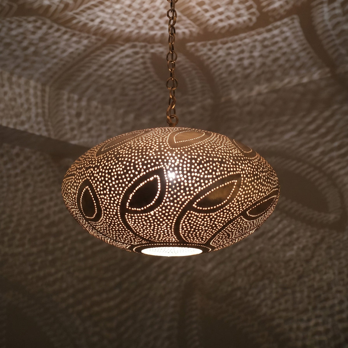 Close detail of the lit Souhail pendant, leafwork pierced through the brass