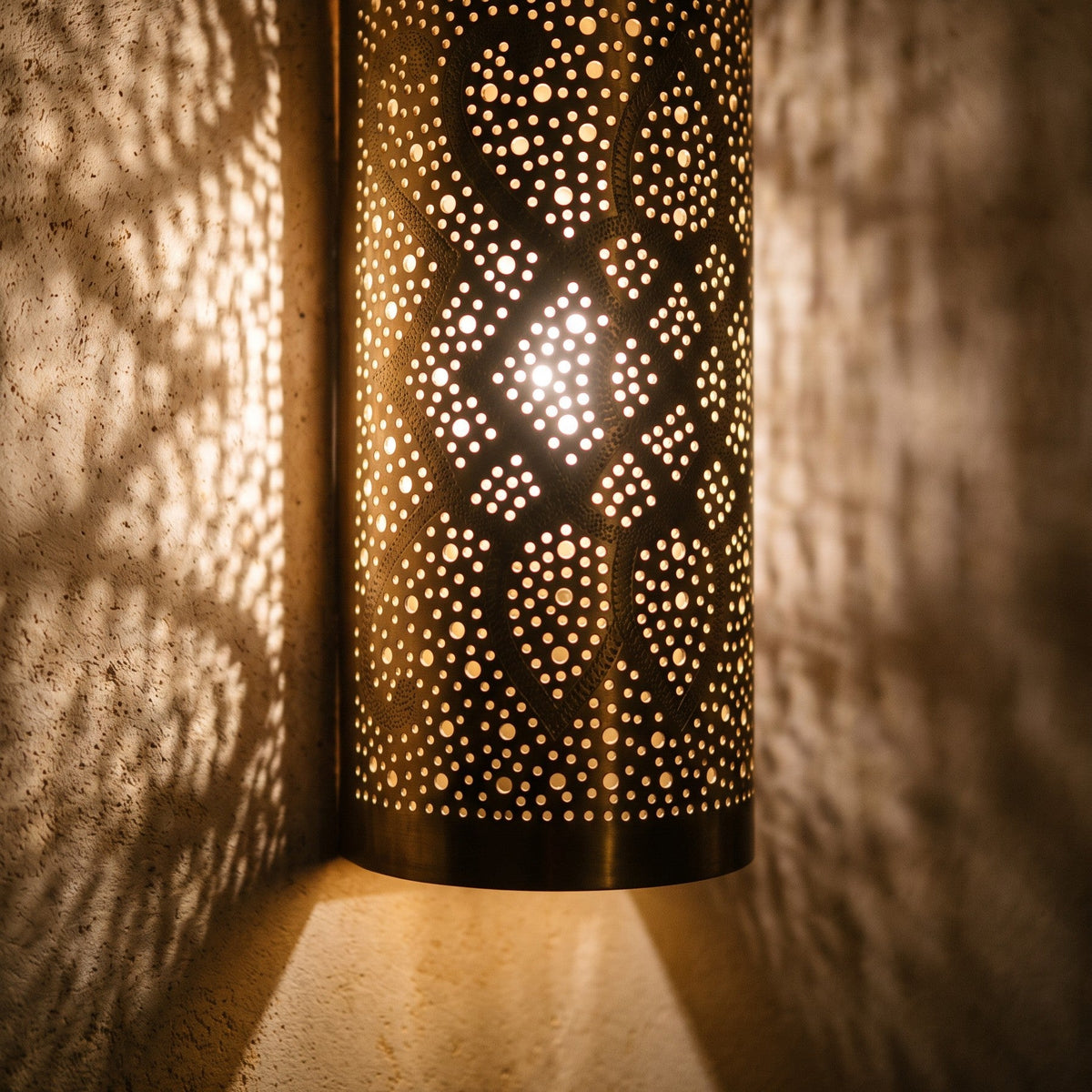 Detail of a lit Sqala sconce, its pierced pattern glowing warm