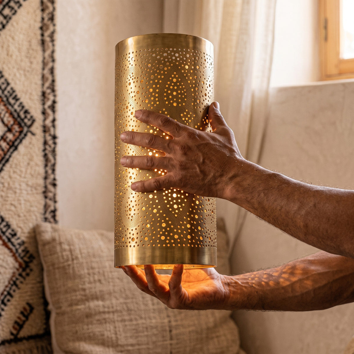 The maker's hands holding a Sqala sconce shade of pierced brass