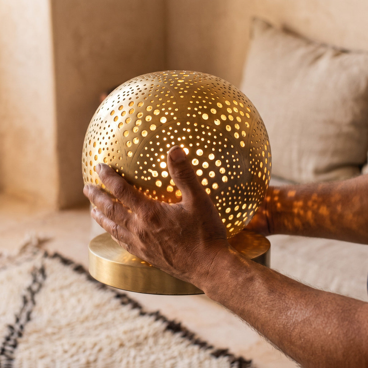 A maalem's hands holding the pierced brass ball of the Tala lamp